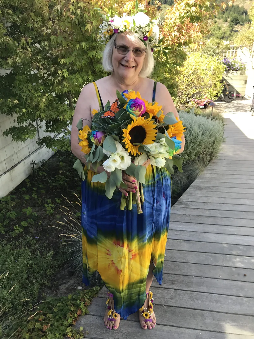 Vicki McFall in a flower crown, holding a bright bouquet of sunflowers and roses