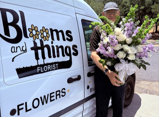 Blooms & Things driver with a purple-and-white bouquet by the branded delivery van